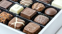 Assorted luxury chocolate pralines and truffles in elegant gift box with dark, milk, and white chocolate varieties featuring decorative patterns and textures.
