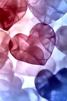 Translucent heart shapes in red, pink and blue tones creating romantic ethereal composition with soft light and shadows. Suitable for Valentine's Day designs.