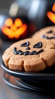 Halloween pumpkin shaped cookies with chocolate chip faces on dark plate with orange bokeh lights background for seasonal baking and party treats.