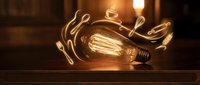 Vintage Edison bulb with glowing filament and swirling light trails on wooden surface against brick wall background for creative lighting design concepts.
