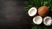 Fresh coconuts split in half showing white flesh with palm leaves on dark wooden background, copy space for tropical food design and menu layouts.