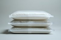 Stack of white sealed plastic bags filled with powder substance on neutral background, packaging concept for food or chemical industry products.