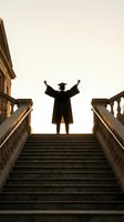 Graduate student celebrating success on stone steps with raised arms at sunset, academic achievement and educational milestone concept.