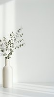 Minimalist eucalyptus branches in white ceramic vase against neutral wall with natural light, suitable for home decor and wellness design projects.