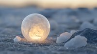 Frozen soap bubble on snow with golden sunrise light glowing through crystallized sphere, creating magical winter macro photography moment in nature.
