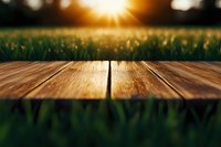 Empty wooden table at sunset with blurred green grass background and sunburst, natural bokeh lights. Suitable for product placement or montage.