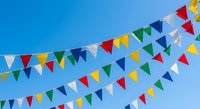 Colorful triangular bunting flags hanging against bright blue sky for outdoor celebrations, festivals, parties and festive decorations.