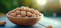 Fresh whole walnuts in wooden bowl on rustic blue table with soft natural lighting and blurred green garden background, healthy snack concept.