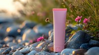 Pink cosmetic tube on natural stone background with pink flowers and soft sunset bokeh light. Organic skincare product photography for beauty brands.