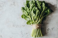 Fresh green spinach bunch tied with rustic twine on light textured concrete background, top view. Raw organic leafy vegetables for healthy eating.