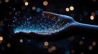 Magical glowing blue particles floating above silhouetted hand against dark background with golden bokeh lights, creating ethereal mystical atmosphere.