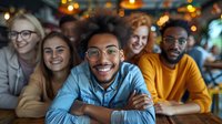 Diverse group of young friends smiling at camera in cozy cafe with warm lighting, showcasing friendship and social connection in casual setting.