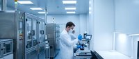 Male scientist in white lab coat working with advanced laboratory equipment in modern sterile research facility with blue lighting and clean room environment.