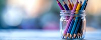Colorful wooden pencils stored in clear glass mason jar against soft blurred background, creating minimalist composition for education and creativity concepts.