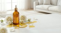 Amber glass dropper bottle with golden oil spill surrounded by white roses on marble surface in bright modern living room interior for skincare and wellness.