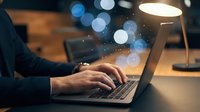 Professional businessman typing on laptop computer with glowing digital particles and bokeh lights in modern office workspace for technology concepts.