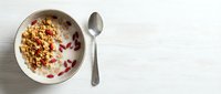 Overhead view of yogurt bowl with granola and berries on white wooden surface with spoon, breakfast or healthy eating concept.