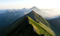 Dramatic mountain ridge with green slopes bathed in morning sunlight, stretching into misty mountain peaks against atmospheric hazy horizon.