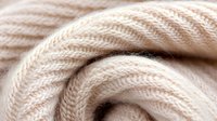 Soft beige knitted wool texture in macro view showing detailed yarn pattern and stitches, creating gentle curves and swirls in neutral tones.