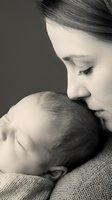 Tender mother gently kissing sleeping newborn baby in intimate black and white portrait capturing maternal love and bonding moment for family photography.
