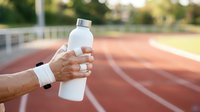 Athlete holding white water bottle on running track during outdoor training session, staying hydrated during sports workout.
