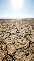 Cracked, parched earth stretches across barren landscape under clear sky, depicting severe drought, desertification, and climate change impacts on arid terrain.