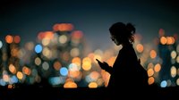 Young woman silhouette using smartphone against blurred city lights at night. Urban lifestyle technology concept for social media and communication designs.