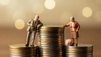 Business partners miniature figures standing on golden coin stacks discussing financial investment strategy with warm bokeh background for wealth concepts.