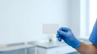 Healthcare professional wearing blue latex gloves holding a blank label or sticker in a clinical laboratory or medical office setting for health communication.