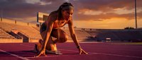 African American female athlete in starting position on track during golden hour sunset training session at stadium.