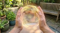 Hands holding glowing transparent sphere with magical light effects in peaceful garden setting for meditation and spiritual wellness concepts.