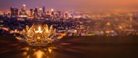 Golden lotus flower candle holder glowing against blurred city skyline at sunset, creating warm ambient lighting for meditation and spiritual practices.