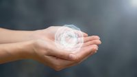 Hands holding glowing circular energy orb with light rays against dark background for spiritual healing and meditation concepts.