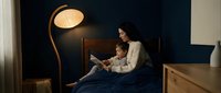 Mother and daughter reading bedtime story together in cozy bedroom with warm lamp lighting creating intimate family bonding moment at night.