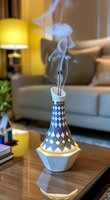 Glowing decorative incense burner with geometric pattern emits delicate smoke trails in modern living room setting, creating peaceful ambiance on wooden table surface.