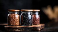 Glass jars with wooden lids filled with different types of quinoa and lentils on rustic wooden board against dark background, moody food photography.