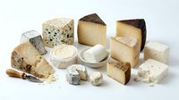Assorted artisanal cheese selection including aged cheddar, blue cheese, and soft varieties with spreads and knife on white background for culinary content.