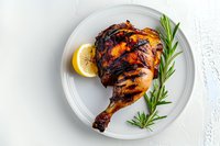 Grilled chicken leg quarter with crispy charred skin served on white plate with fresh rosemary sprig and lemon slice, captured on light background.