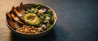 Healthy Buddha bowl with grilled chicken, avocado, chickpeas and mixed greens on wooden table for nutritious meal planning and clean eating lifestyle.