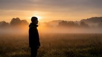 Person silhouette standing in misty field during golden sunrise with warm light and peaceful morning atmosphere for meditation and mindfulness concepts.