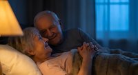 Elderly couple sharing intimate moment in bed at night, senior man comforting woman with warm lighting creating romantic atmosphere for healthcare concepts.