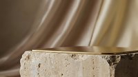 Luxury gold podium on travertine stone with flowing silk fabric background for premium product display and cosmetic presentation.