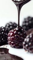 Dark chocolate sauce dripping onto fresh blackberry against white background, macro shot showing glossy texture and rich details of berry and melted chocolate.