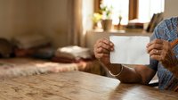 Senior male with brown skin tone holding blank white card at wooden table indoors, suitable for messaging, advertising, and promotional campaigns.