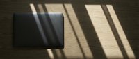 Black laptop on wooden floor with sunlight casting window shadows across surface, suitable for business and technology concepts.