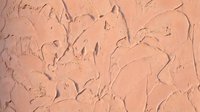 Textured peach coral stucco wall surface with rough plaster finish and natural imperfections for interior design and architectural backgrounds.
