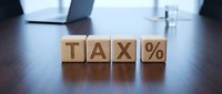 Tax percentage symbol displayed on wooden blocks on office desk with laptop and glass of water in background.
