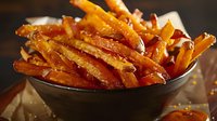 Crispy sweet potato fries seasoned with herbs and spices served in black ceramic bowl, golden brown with caramelized edges on dark background with natural lighting.