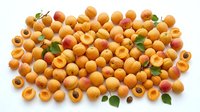 Fresh organic apricots scattered on white background with green leaves and cut halves showing pits, perfect for healthy food designs and recipes.