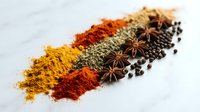 Colorful spice collection with turmeric, paprika, herbs, star anise and peppercorns arranged in rows on white background for culinary cooking and seasoning.